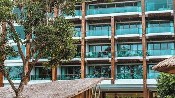 Un edificio de varios pisos con ventanas grandes y balcones, rodeado de árboles y una estructura de techo de paja.