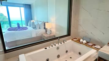 Un baño moderno con una bañera grande, un espejo y vistas a un dormitorio con cama y ventana.