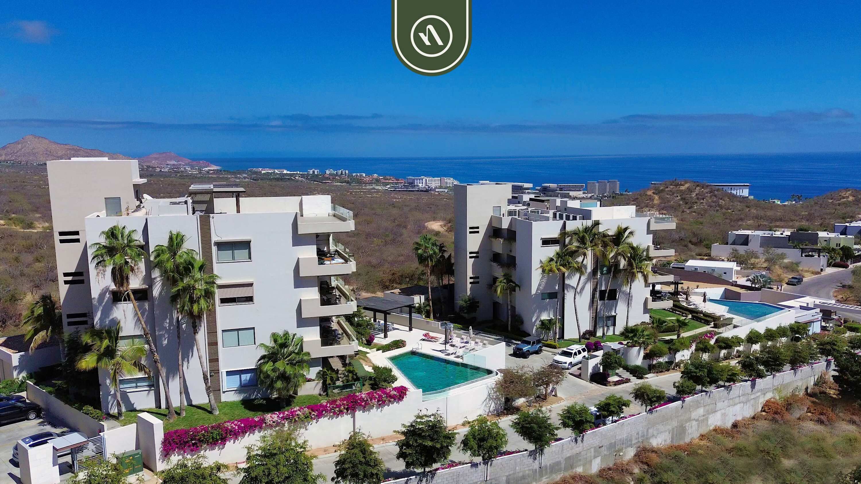 A modern resort with multiple buildings, a swimming pool, and a view of the ocean.