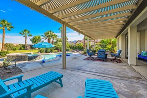 Un área de patio techada con sillones reclinables azules, una piscina y una sombrilla.