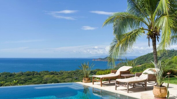 An infinity pool with a clear view of the ocean and hills.
