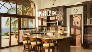 A kitchen with a large island, bar stools, and a view of the ocean.
