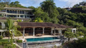 A large house with a swimming pool, surrounded by lush greenery and hills.