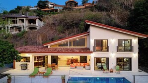 Ein modernes, zweistöckiges Haus mit Swimmingpool, großen Fenstern und einer Terrassenfläche.