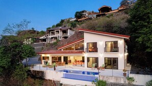 Ein modernes, zweistöckiges Haus mit Pool, großen Fenstern und einem Balkon.