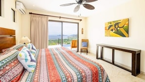 Ein Schlafzimmer mit einem großen Bett, einem Deckenventilator, Blick auf die Landschaft und einem Bild an der Wand.