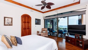 A bedroom with a large bed, a wooden ceiling, a ceiling fan, a TV, and a sliding glass door leading to a balcony with a view. - Playa Hermosa Villa • 3BR • Infinity Pool & Swim-Up Bar • Ocean Views (Playa Hermosa)