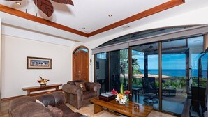 A spacious living room with leather sofas, a wooden coffee table, and a large glass door leading to a balcony with a view of the ocean. - Playa Hermosa Villa • 3BR • Infinity Pool & Swim-Up Bar • Ocean Views (Playa Hermosa)