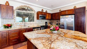 A kitchen with dark wooden cabinets, a granite countertop, a stainless steel refrigerator, and a window with a view of trees. - Playa Hermosa Hillside Villa • 5BR • Sleeps 12 • Infinity Pool & Bay View • Casa Ilan Ilan (Playa Hermosa)