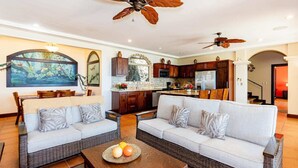 A spacious living room with two sofas, a coffee table, and a dining area with a table and chairs. There is a kitchen area with wooden cabinets and a refrigerator. - Playa Hermosa Hillside Villa • 5BR • Sleeps 12 • Infinity Pool & Bay View • Casa Ilan Ilan (Playa Hermosa)