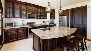 A modern kitchen with dark wood cabinets, stainless steel appliances, a granite countertop, and pendant lighting.