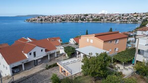 Un quartier résidentiel situé sur la côte, avec des maisons aux toits recouverts de tuiles rouges, une rue pavée et une vue sur la mer.