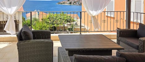 Een balkon met rieten meubilair, witte gordijnen en uitzicht op zee.