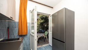 Una cocina funcional con refrigerador de acero inoxidable, una mesa de comedor con sillas y un ventanal corredizo que da a un espacio exterior.