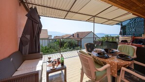 Un balcón con mesa lista para dos personas, un sofá de mimbre y vistas al mar.