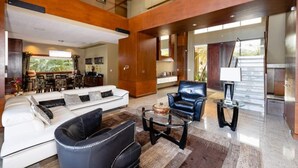 A spacious living area with a white sofa, black leather armchair, and a glass coffee table.