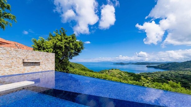 A infinity pool with a clear view of the sea and hills.