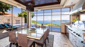 A spacious patio with a glass table, wicker chairs, a grill, and a view of the ocean.