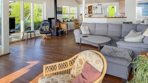 A spacious living room with a grey sofa, a wicker chair, a small table, and a fireplace. - Stunning home in Ebeltoft with sauna (Ebeltoft)