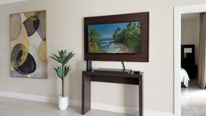 Ein Hotelzimmer mit einem an einer dunklen Kommode befestigten Fernseher, einer Zimmerpflanze und einem Bild an der Wand.