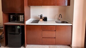 Une cuisine compacte avec des meubles en bois, un four à micro-ondes encastré, un réfrigérateur noir, un évier et un plan de travail équipé d’ustensiles de cuisine.