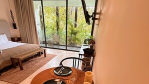 Une chambre moderne avec un grand lit, une table à manger dressée pour deux personnes et un balcon offrant une vue sur la verdure.