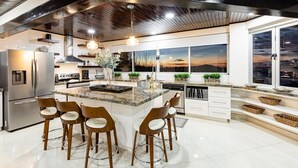 A modern kitchen with a central island, stainless steel appliances, and a large window offering a view of the cityscape. - Playa Hermosa Villa • 4BR • Infinity Pool • Ocean & Bay View • Recently Renovated • Sunset Ridge (Playa Hermosa)