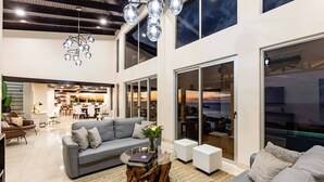 A spacious living area with a grey sofa, a coffee table, and a view of the ocean through large sliding glass doors. - Playa Hermosa Villa • 4BR • Infinity Pool • Ocean & Bay View • Recently Renovated • Sunset Ridge (Playa Hermosa)