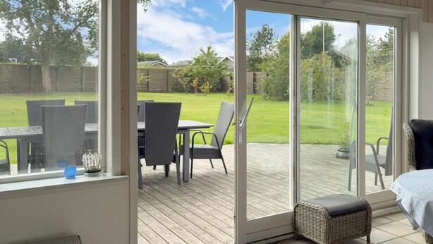 A sunlit patio with a table and chairs, a wicker sofa, and a sliding glass door leading to a grassy backyard.
