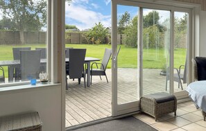 A sunlit patio with a table and chairs, a wicker sofa, and a sliding glass door leading to a grassy backyard. - Awesome home in Hadsund with WiFi (Hadsund)