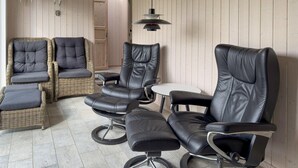 A room with three black leather chairs and two wicker sofas with grey cushions.