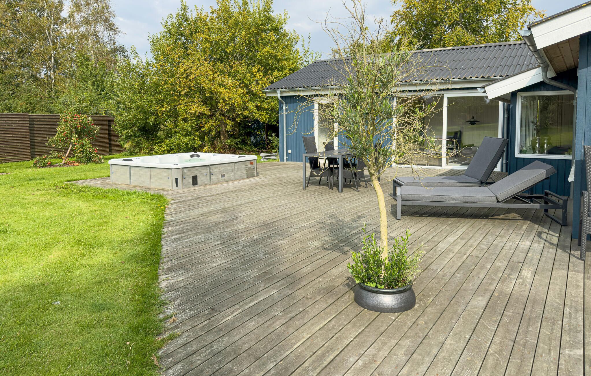 Une terrasse en bois avec un jacuzzi, des sièges d’extérieur et une plante en pot.