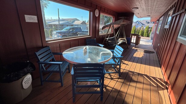 Une terrasse en bois avec une table en verre et des chaises bleues, donnant sur un quartier résidentiel.
