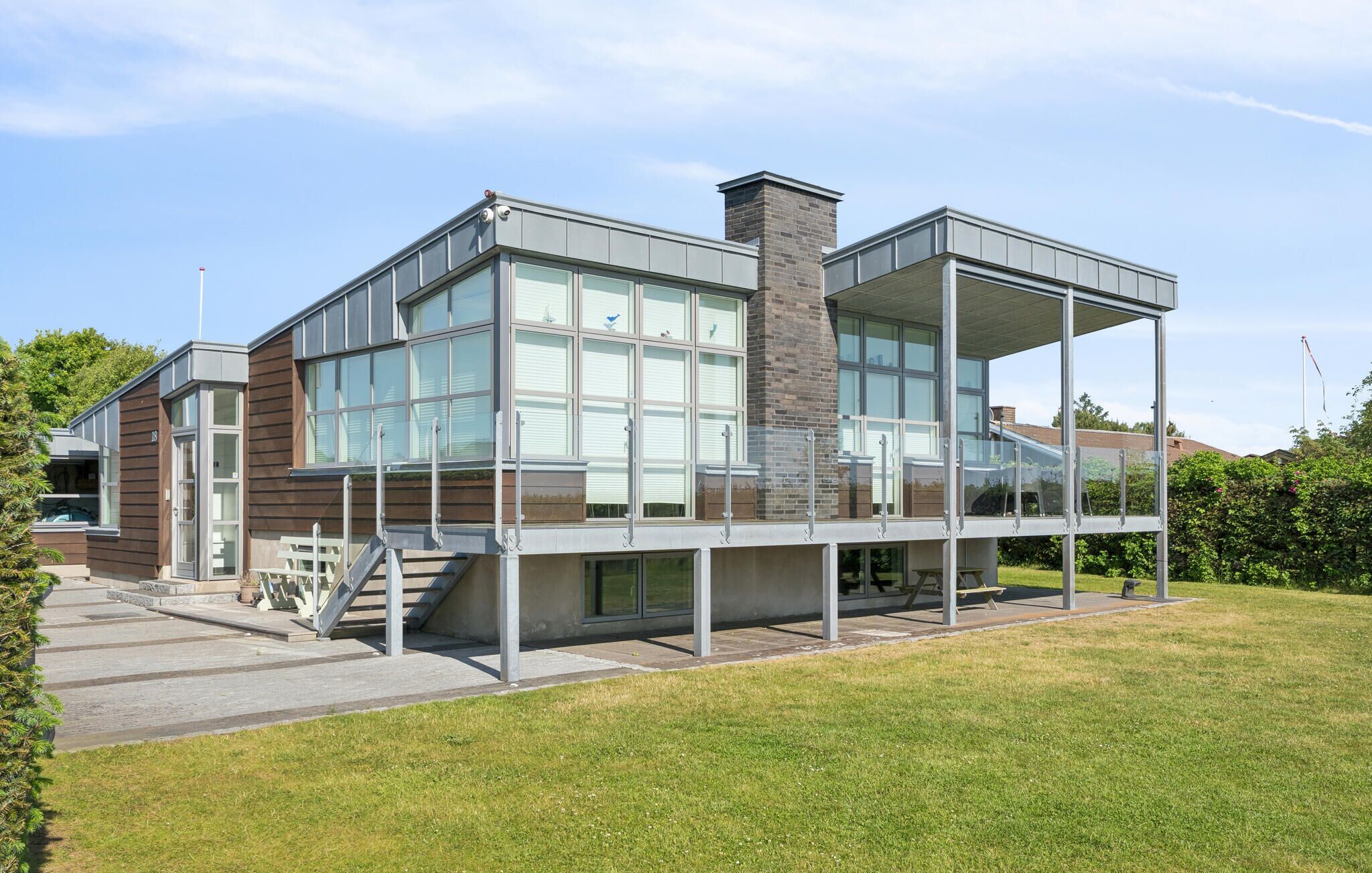 A modern building with large windows, a brick chimney, and a covered outdoor area with a staircase.