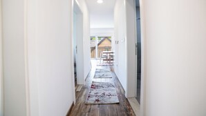 Un couloir étroit, doté d’un plancher en bois et de murs blancs, mène à un coin repas avec une table et des chaises.