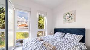 Une chambre avec un grand lit, une vue sur l’extérieur grâce à une porte coulissante, et un tableau accroché au mur.