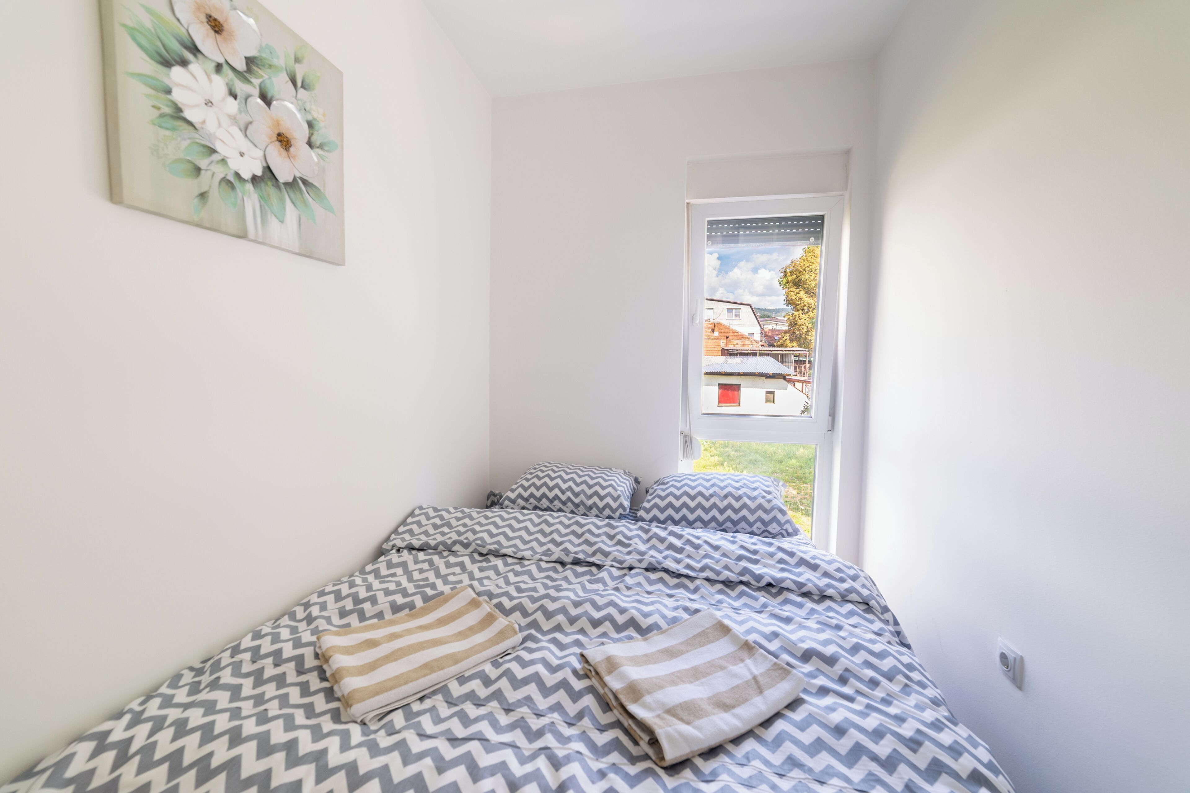 Una camera da letto con un letto, cuscini e una finestra che si affaccia su edifici.