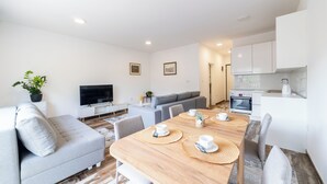 Un salon moderne avec un canapé, un téléviseur et une table à manger agrémentée de sets de table.