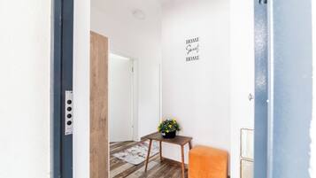 A hallway with a wooden floor, a small table with a potted plant, a bench, and a wall sign that says "HOME Sweet HOME".