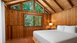Een slaapkamer met houten lambrisering, een groot bed, een raam met luiken en een nachtkastje met een lamp.