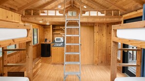 Une cabane en bois avec des lits superposés, un coin cuisine et une échelle menant au lit supérieur.