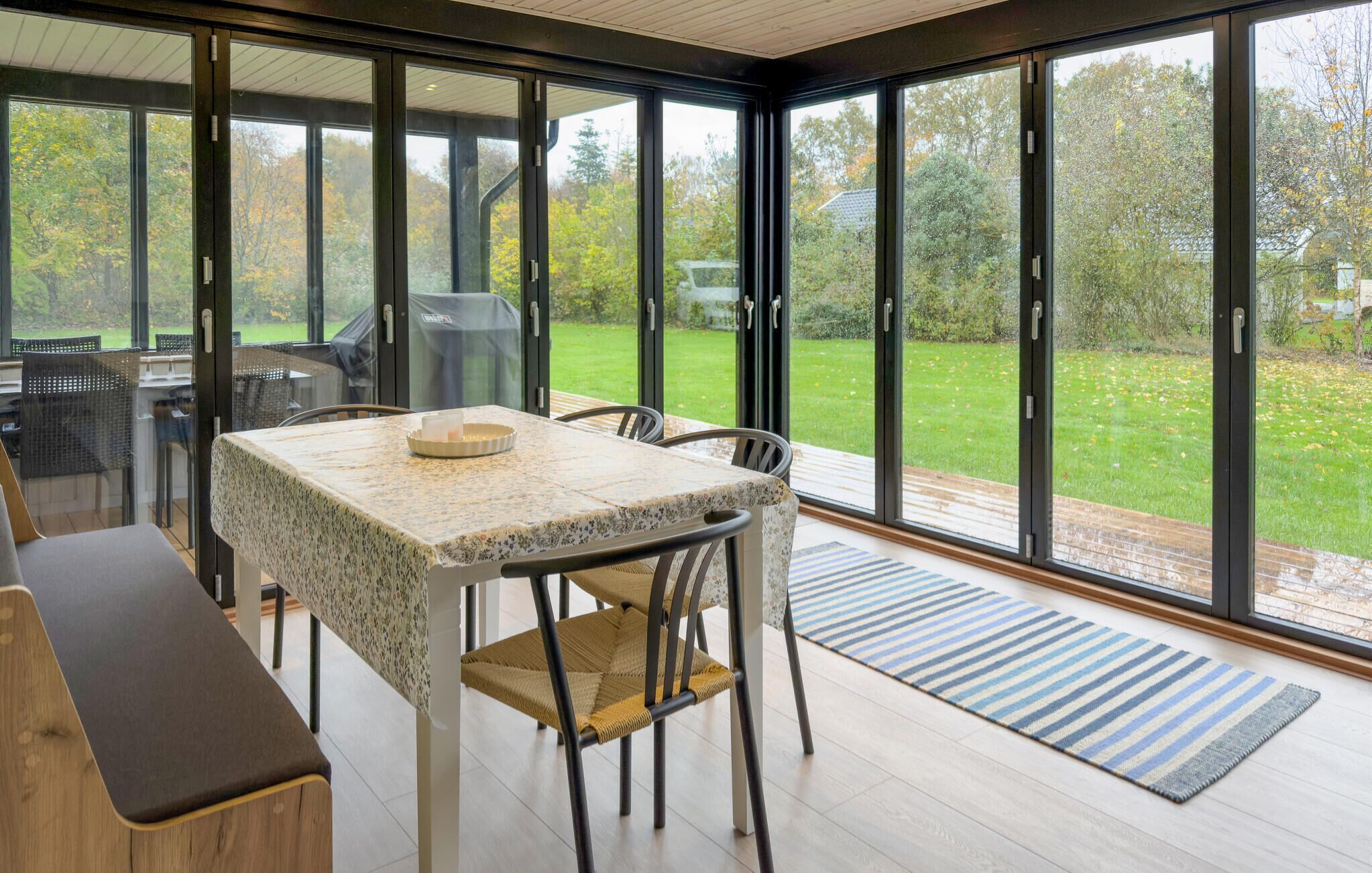A conservatory with a table and chairs, large glass doors, and a view of a green garden.
