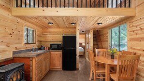 L’intérieur d’un chalet en bois comprend une cuisine, un coin repas et une chambre à coucher visible.