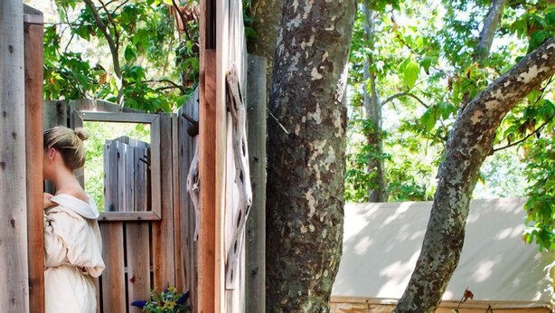 A wooden deck with a rustic wooden structure, a tree, and a tent in the background. - Central Cabin + Queen + Firepit | No Hidden Fees (Santa Barbara)