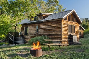 Eine rustikale Blockhütte mit Feuerstelle, Holzstufen und einem Picknicktisch.