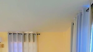 A room with a sofa, a standing mirror, a lamp, and a window with curtains. - Oceanview Suites (St. George's)