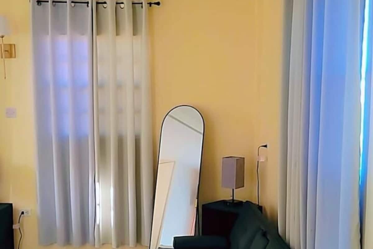 A room with a sofa, a standing mirror, a lamp, and a window with curtains.