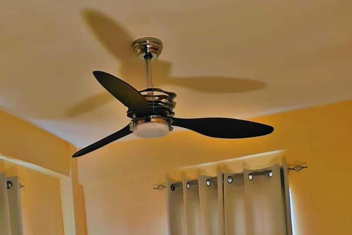 A hotel room with a bed, a ceiling fan, and curtains.