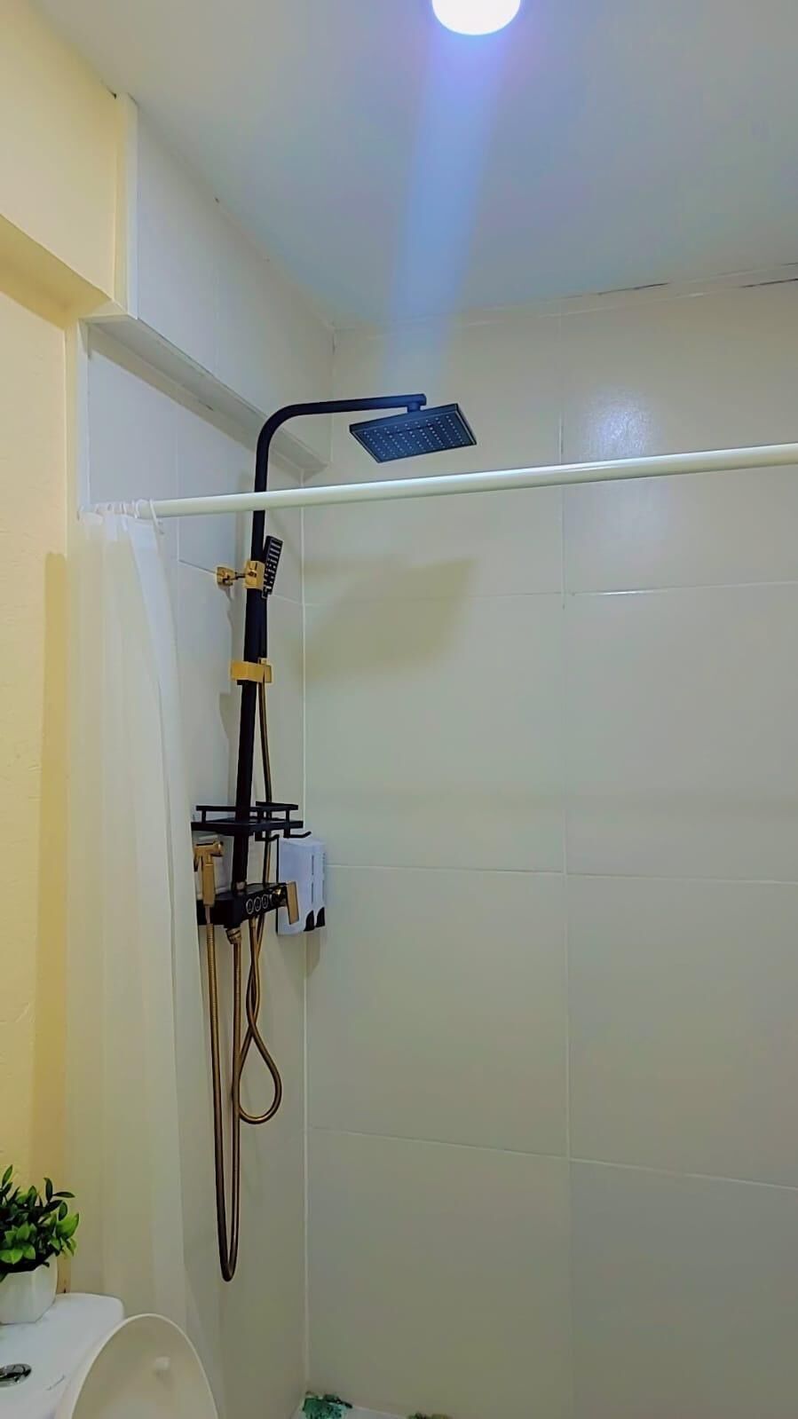 A shower with a handheld showerhead, a wall-mounted control panel, and a visible water pipe.