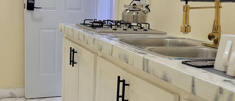 A kitchen with a white door marked with the number 9, a gas stove, a sink with a gold faucet, and black and white patterned mats on the floor.